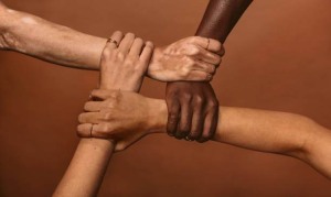 Four diverse women holding each others wrists in a circle. Top view of female hands linked in the lock against brown background.